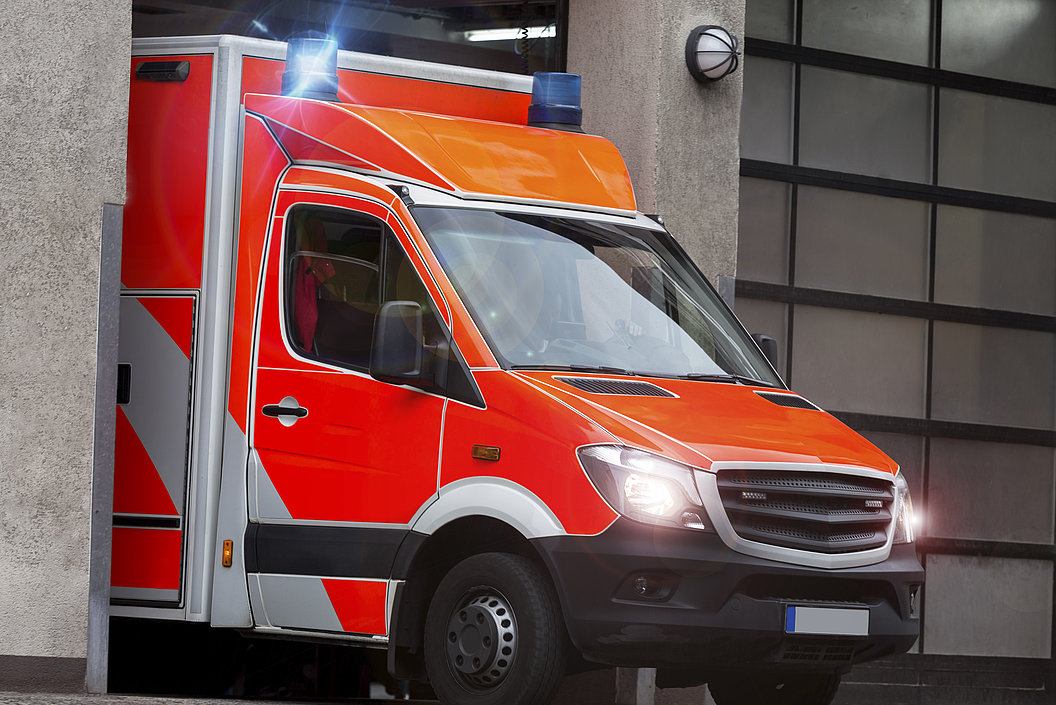 Rotes Rettungsfahrzeug mit eingeschaltetem Blaulicht fährt aus einer Garage.